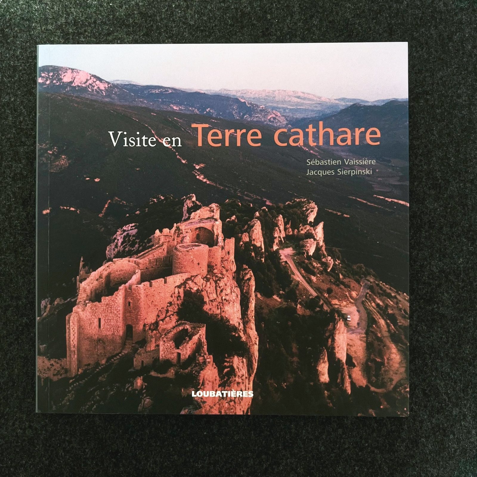 Couverture d'un livre avec une image d'un château en ruines sur une colline, sur fond de montagnes au coucher du soleil