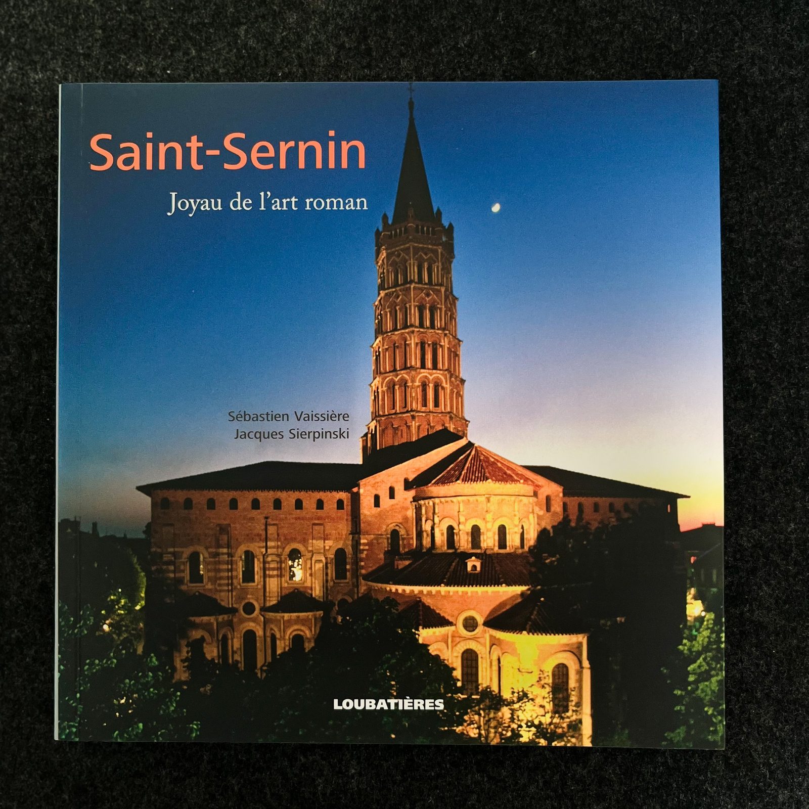 Couverture d'un livre avec une photo de l'église Saint-Sernin illuminée la nuit et un ciel étoilé de fond.
